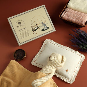 Baby pillow product including a knitted toy, blanket, and card on a brown surface.