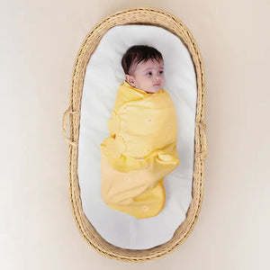Baby swaddled in yellow cloth lying in a wicker basket with a white mattress. Nintara Organic Cotton Wake Me Not Swaddle  0-3 Months Butter Blossoms Go Littles product main image
