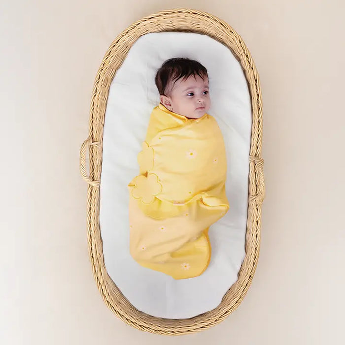 Baby swaddled in yellow cloth lying in a wicker basket with a white mattress. Nintara Organic Cotton Wake Me Not Swaddle  0-3 Months Butter Blossoms Go Littles product main image